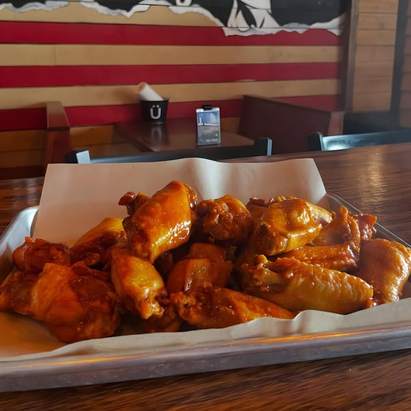 A tray of saucy chicken wings on a wooden table with a red and tan striped wall in the background.