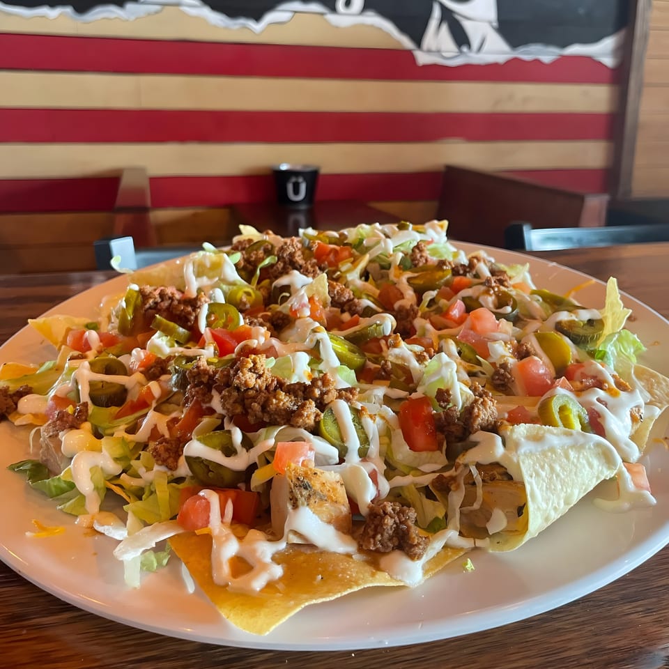 A large plate of FIVE BUCKS DRINKERY nachos with ground beef, lettuce, tomatoes, and jalapeños.
