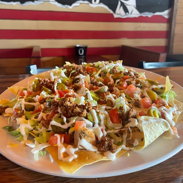 A large plate of FIVE BUCKS DRINKERY nachos with ground beef, lettuce, tomatoes, and jalapeños.