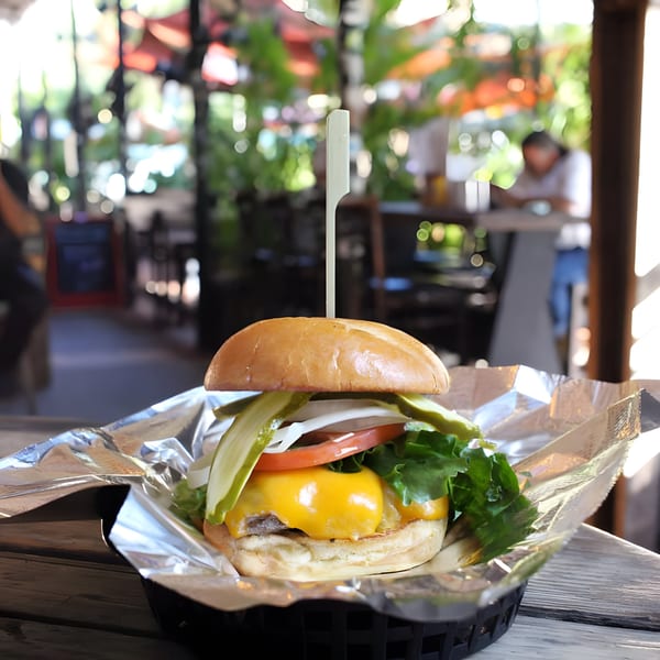 A cheeseburger with lettuce, tomato, onion, and pickles in a basket on a wooden table.