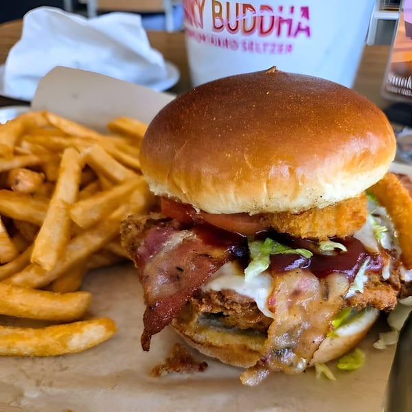 A Five Bucks Drinkery burger with bacon, onion rings, and sauce, served with golden fries.