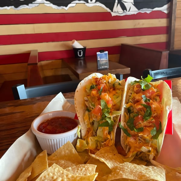 Two tacos with lettuce, cheese, and salsa, served with tortilla chips and a side of salsa.
