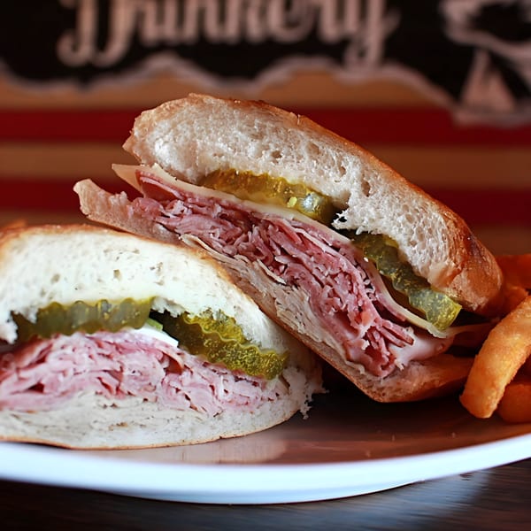 A large deli sandwich with ham, cheese, and pickles, served with fries.